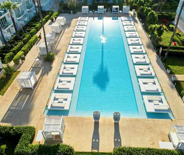 Et rektangulært basseng omgitt av solsenger og grøntområder. (AI-generert tekst)