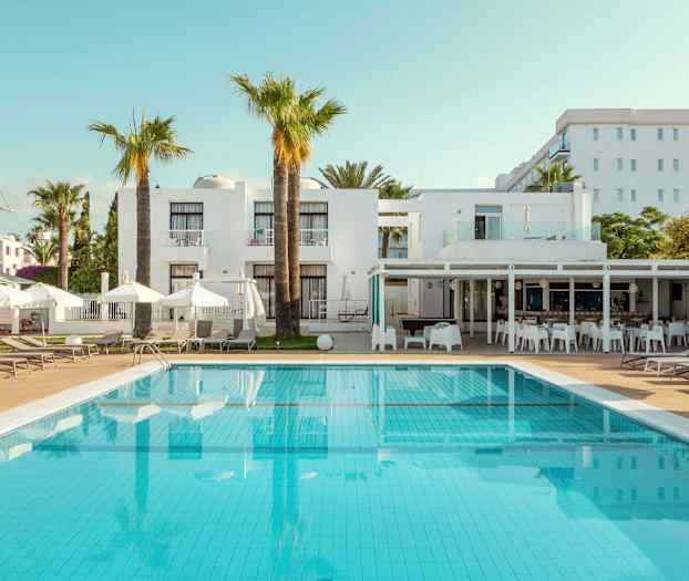 Bilde av hotellbasseng med solsenger og hvite bygninger i bakgrunnen. (AI-generert tekst)