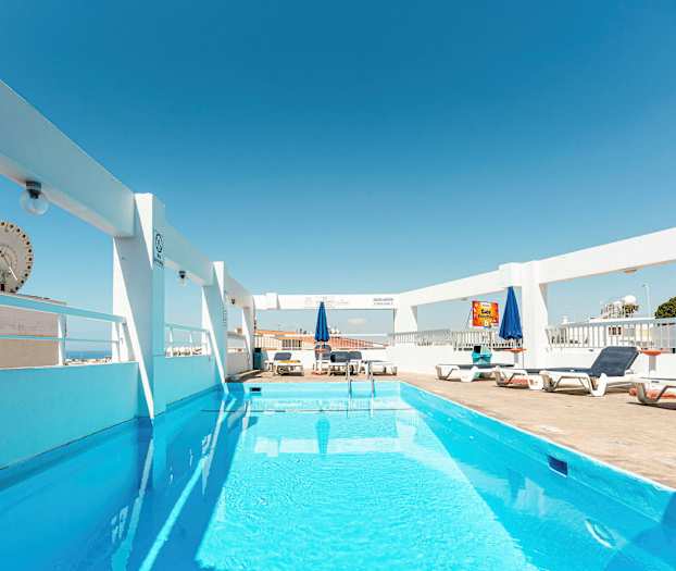 Et utendørsbasseng med solsenger og parasoller under en klar blå himmel. (AI-generert tekst)