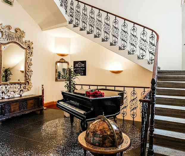 En trapp med et spiralformet rekkverk, et piano, en globus og et stort dekorativt speil. (AI-generert tekst)