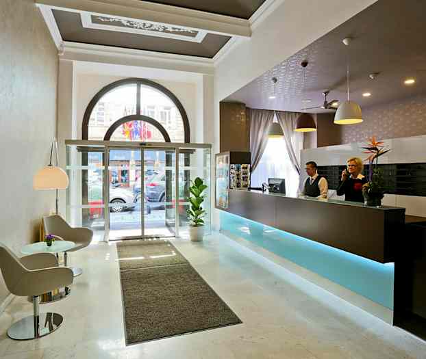 Hotellobby med resepsjon, sittegruppe og glassdører mot utsiden. (AI-generert tekst)