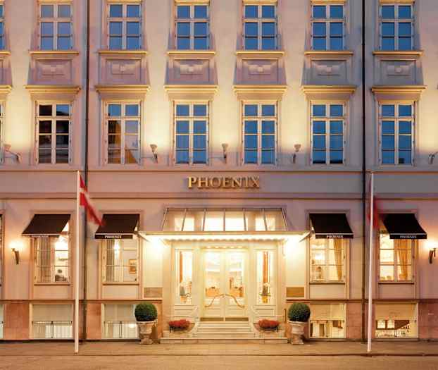 Bildet viser en eksteriør av et hotell med en opplyst inngang og klassisk fasade. (AI-generert tekst)