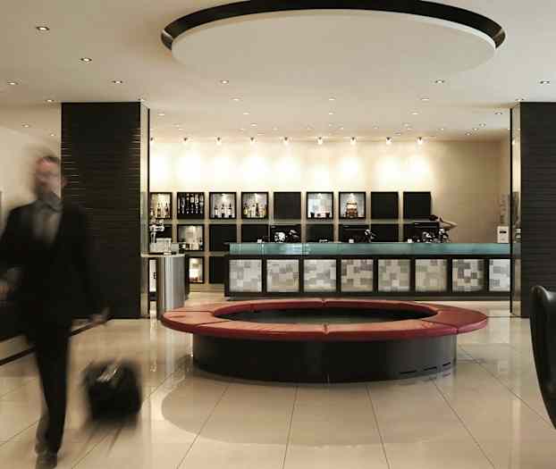 En godt opplyst hotellobby med en resepsjon, moderne sitteplasser og et rundt sofahjørne. En person med bagasje er i bevegelse. (AI-generert tekst)