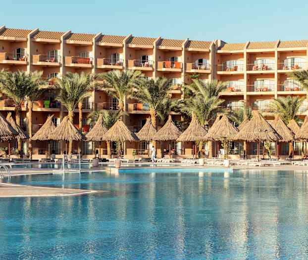 En hotellbygning med balkonger, foran et basseng og palmer. (AI-generert tekst)