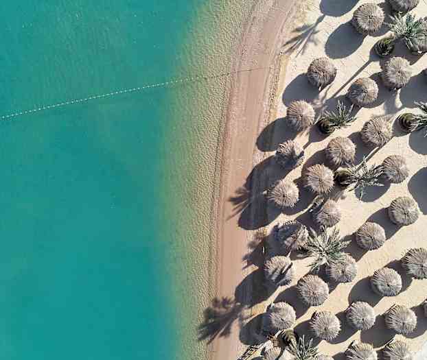 Luftbilde av en sandstrand med turkis vann og parasoller. (AI-generert tekst)