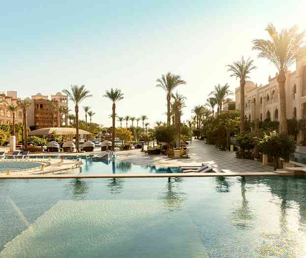 Hotellområde med utendørsbassenger og rader av palmer ved siden av bygninger. (AI-generert tekst)