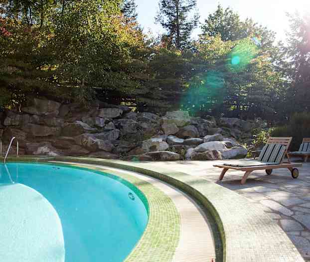 Et basseng omgitt av solsenger og grønn natur. (AI-generert tekst)