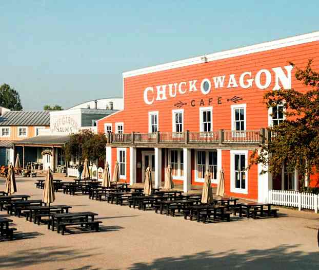 Et område med bord og parasoller foran en bygning med skiltet 'Chuck Wagon Cafe'. (AI-generert tekst)