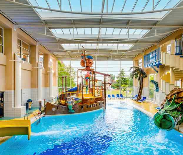 Et innendørsbasseng med et piratskip og vannsklier, omgitt av solsenger og planter. (AI-generert tekst)