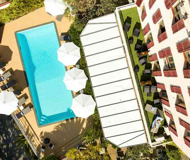 Bilde av et basseng, solsenger og parasoller ved siden av en bygning. (AI-generert tekst)