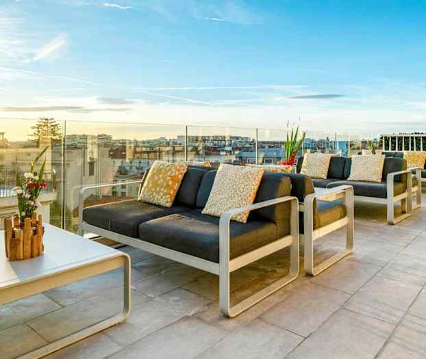 Møblert takterrasse med utsikt over byen og solnedgangen. (AI-generert tekst)