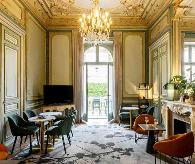 Et elegant møblert rom med dekorert tak, sittegrupper og en lysekrone. (AI-generert tekst)