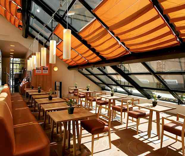 En lys og moderne spisesal med tremøbler, oransje takdekorasjoner og store vinduer. (AI-generert tekst)