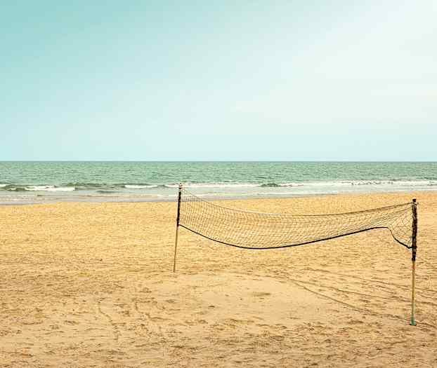 En tom sandstrand med et oppsatt volleyballnett og havet i bakgrunnen. (AI-generert tekst)