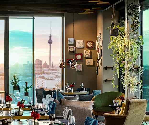 Et elegant restaurantinteriør med moderne møbler, grønne planter og utsikt over en bysilhuett med et landemerke i bakgrunnen. (AI-generert tekst)