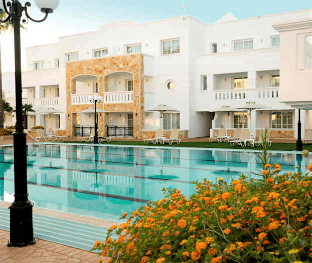 Hotellbygning med basseng og omkringliggende solsenger. (AI-generert tekst)