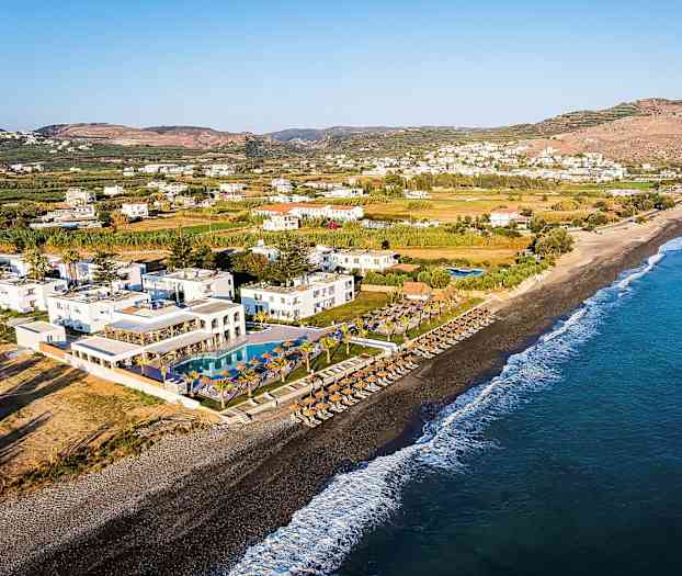 Utsikt over en strand med parasoller, solsenger og et resort med bassenger i nærheten. (AI-generert tekst)