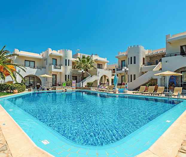 Et basseng omgitt av solsenger og parasoller foran bygninger med hvit fasade og unike arkitektoniske detaljer. (AI-generert tekst)