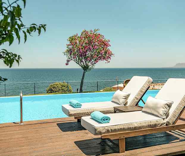 To solsenger ved et basseng med utsikt over havet. (AI-generert tekst)