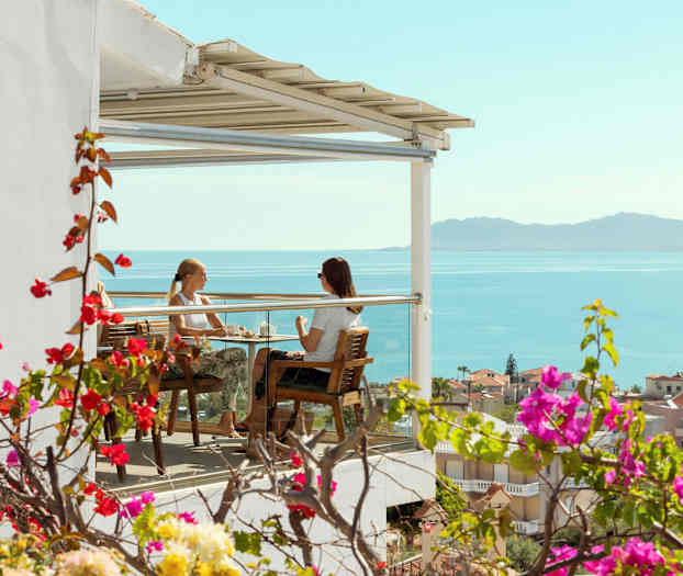 To personer sitter på en terrasse med utsikt over havet. (AI-generert tekst)