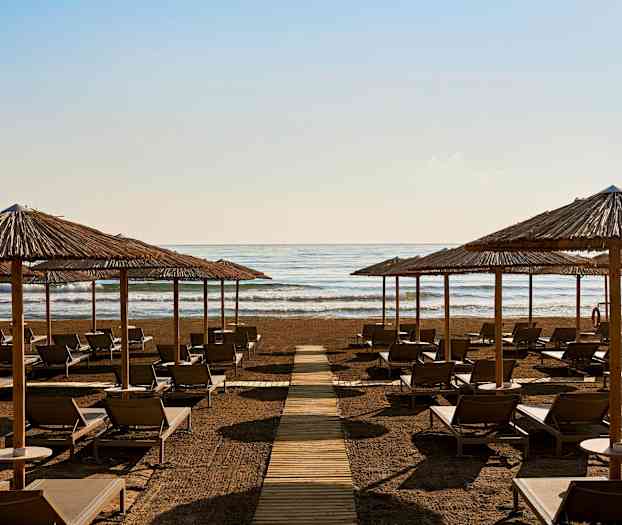 Solstoler og parasoller på en strand foran havet. (AI-generert tekst)