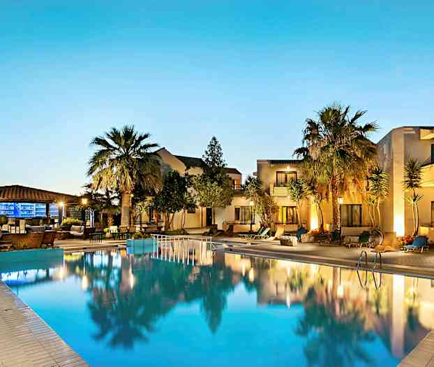 Et opplyst svømmebasseng foran et hotell med palmer og uteplass i skumringen. (AI-generert tekst)