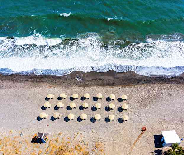 Flyfoto av en strand med parasoller og bølger. (AI-generert tekst)