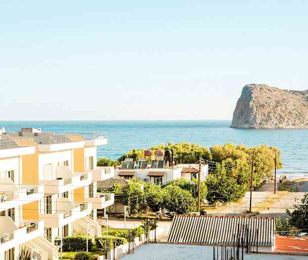 Utsikt over bygninger, grøntområder og havet med en klippe i bakgrunnen. (AI-generert tekst)