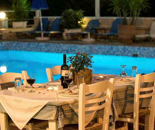 Et dekket bord med hvite stoler ved siden av et opplyst basseng. (AI-generert tekst)