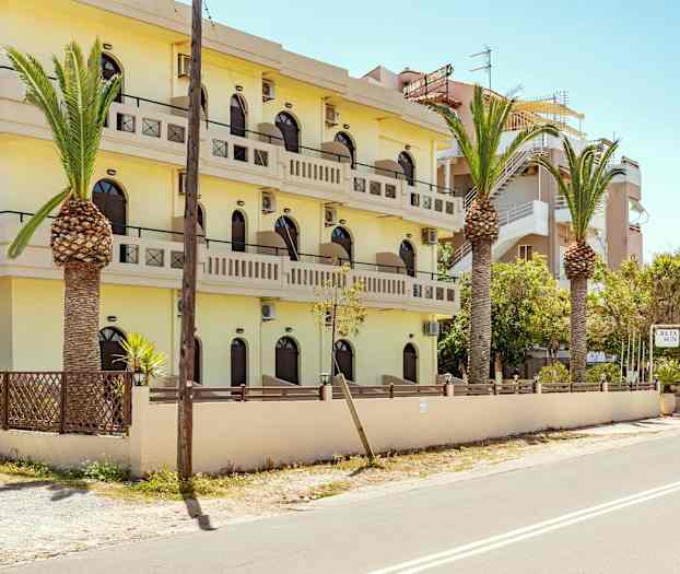 En gul bygning med flere etasjer og balkonger, omgitt av palmer og en vei. (AI-generert tekst)