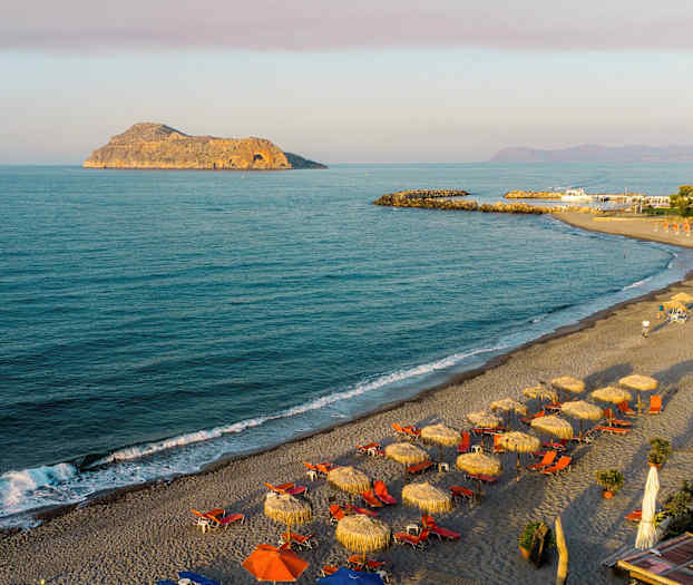 Strand med parasoller og solsenger ved havet. Klippe i bakgrunnen. (AI-generert tekst)
