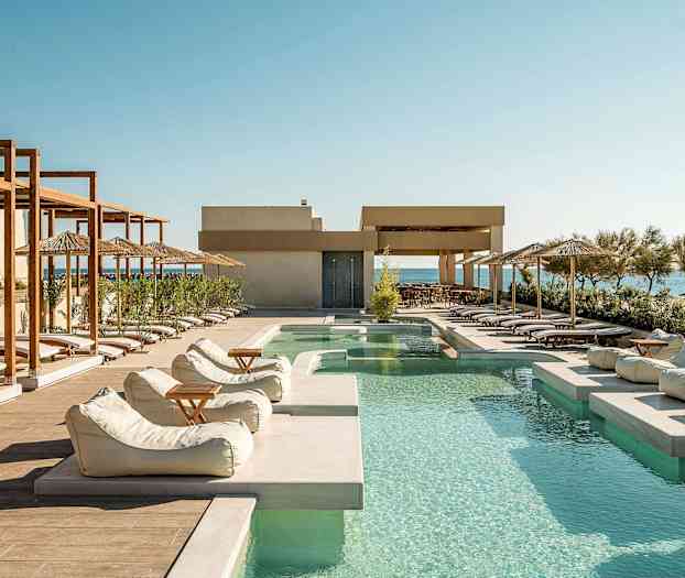 Utendørsbasseng med solsenger og parasoller langs kanten, med havet i bakgrunnen. (AI-generert tekst)