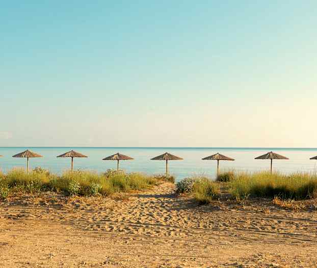 Strand med syv strandparasoller på rad og hav i bakgrunnen. (AI-generert tekst)