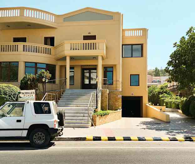 En bil står parkert foran en bygning med et skilt med teksten 'Achilles Plaza'. (AI-generert tekst)