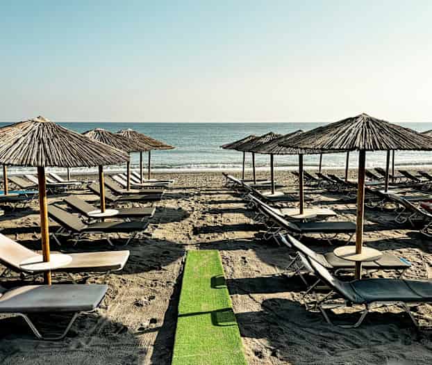 Strand med solsenger og parasoller på rad ved sjøen. (AI-generert tekst)