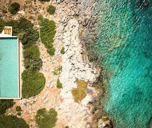 Et basseng ved siden av klipper og hav sett ovenfra. (AI-generert tekst)