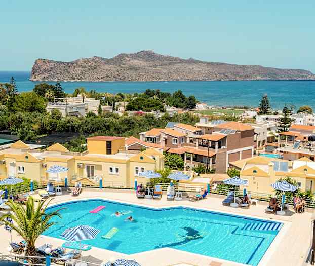 Et basseng med solsenger og parasoller foran en utsikt som inkluderer hus, grøntområder og hav. (AI-generert tekst)