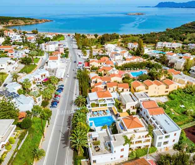 Luftfoto av en kystby med hus, bassenger og havet i bakgrunnen. (AI-generert tekst)