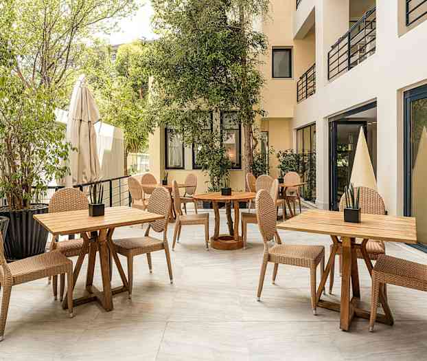 Utendørsområde med bord og stoler omgitt av vegetasjon. (AI-generert tekst)