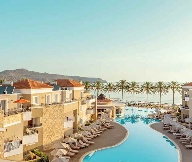 Oversikt over en resort med basseng og solsenger, med havutsikt og palmer i bakgrunnen. (AI-generert tekst)