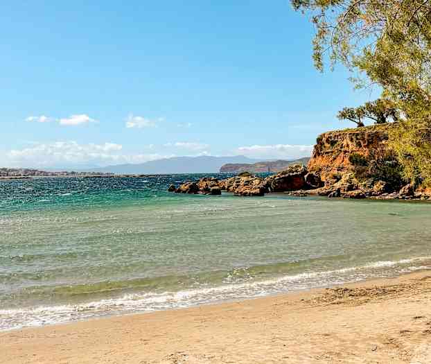 Sandstrand med turkis hav, steinklipper og grønne trær. (AI-generert tekst)