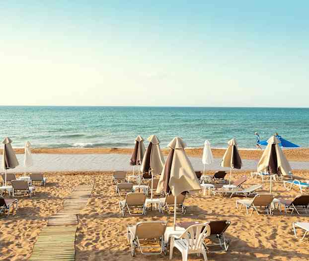 Solstoler og parasoller er plassert på en sandstrand med havet i bakgrunnen. (AI-generert tekst)