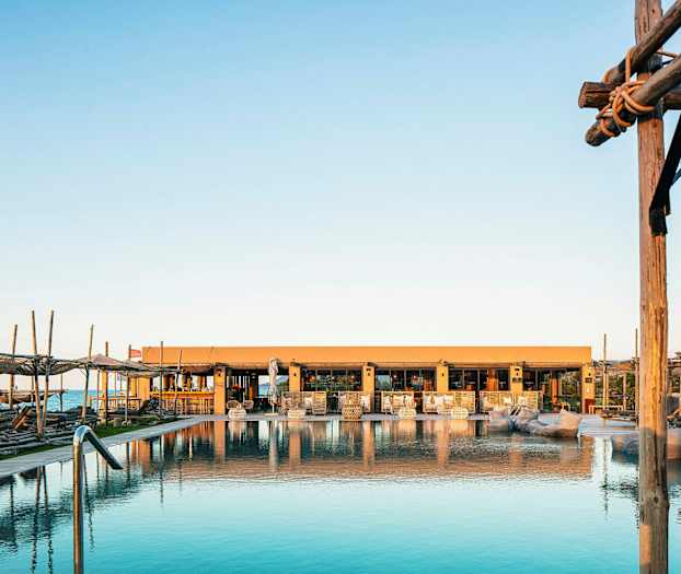 Bilde av et basseng med solsenger og et hus i bakgrunnen ved soloppgang eller solnedgang. (AI-generert tekst)