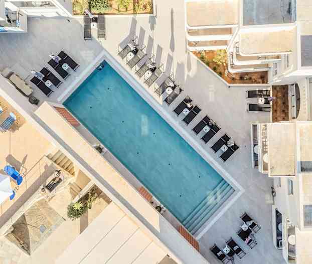 Flyfoto av et utendørs basseng omgitt av solsenger og bord. (AI-generert tekst)