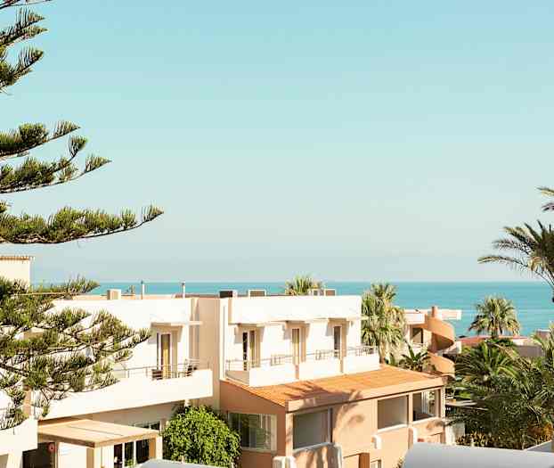 Utsikt over trær, bygninger og havet under en klar himmel. (AI-generert tekst)