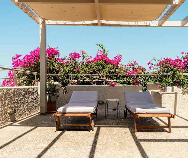 Terrasse med to solsenger, bougainvillea og overheng under blå himmel. (AI-generert tekst)