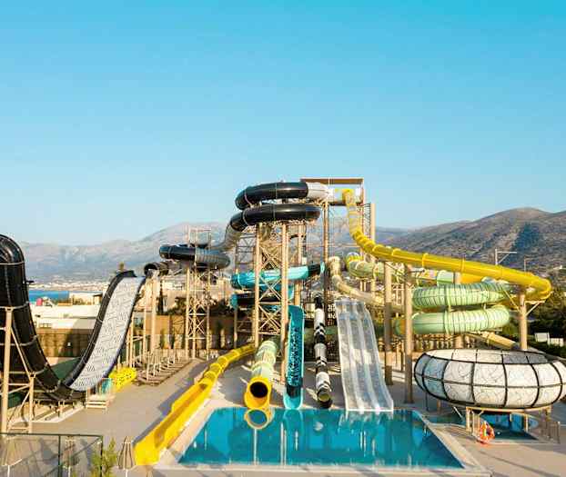 Vannpark med ulike sklier og bassenger foran en fjellaktig bakgrunn. (AI-generert tekst)