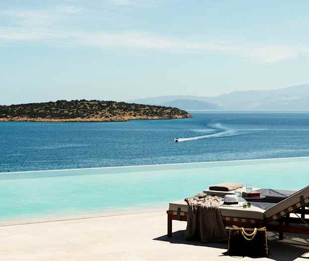 Solstoler ved et infinitybasseng med utsikt over havet og en liten øy. (AI-generert tekst)