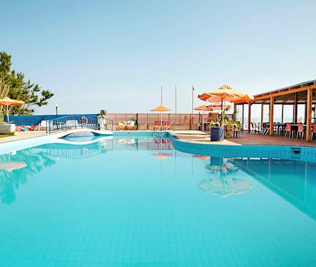 Et utendørs svømmebasseng med parasoller og bord ved siden av. (AI-generert tekst)