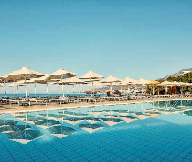 Solstoler og parasoller ved et basseng med utsikt over havet. (AI-generert tekst)